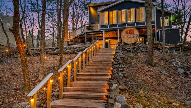 Un escalier en bois mène à une maison moderne dotée d’une terrasse, qui est entourée d’arbres et de rochers.