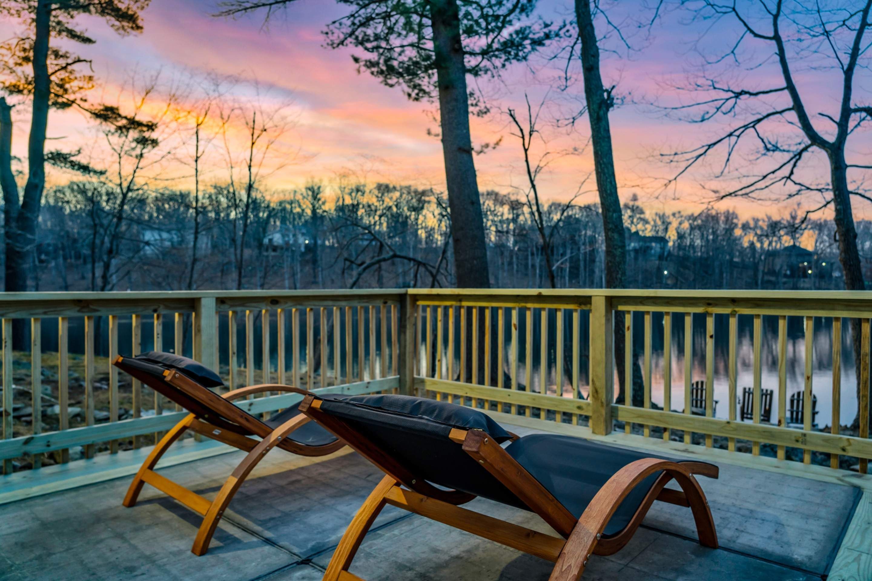 Une terrasse en bois avec deux chaises longues donnant sur une étendue d’eau, entourée d’arbres et d’une rambarde en bois.