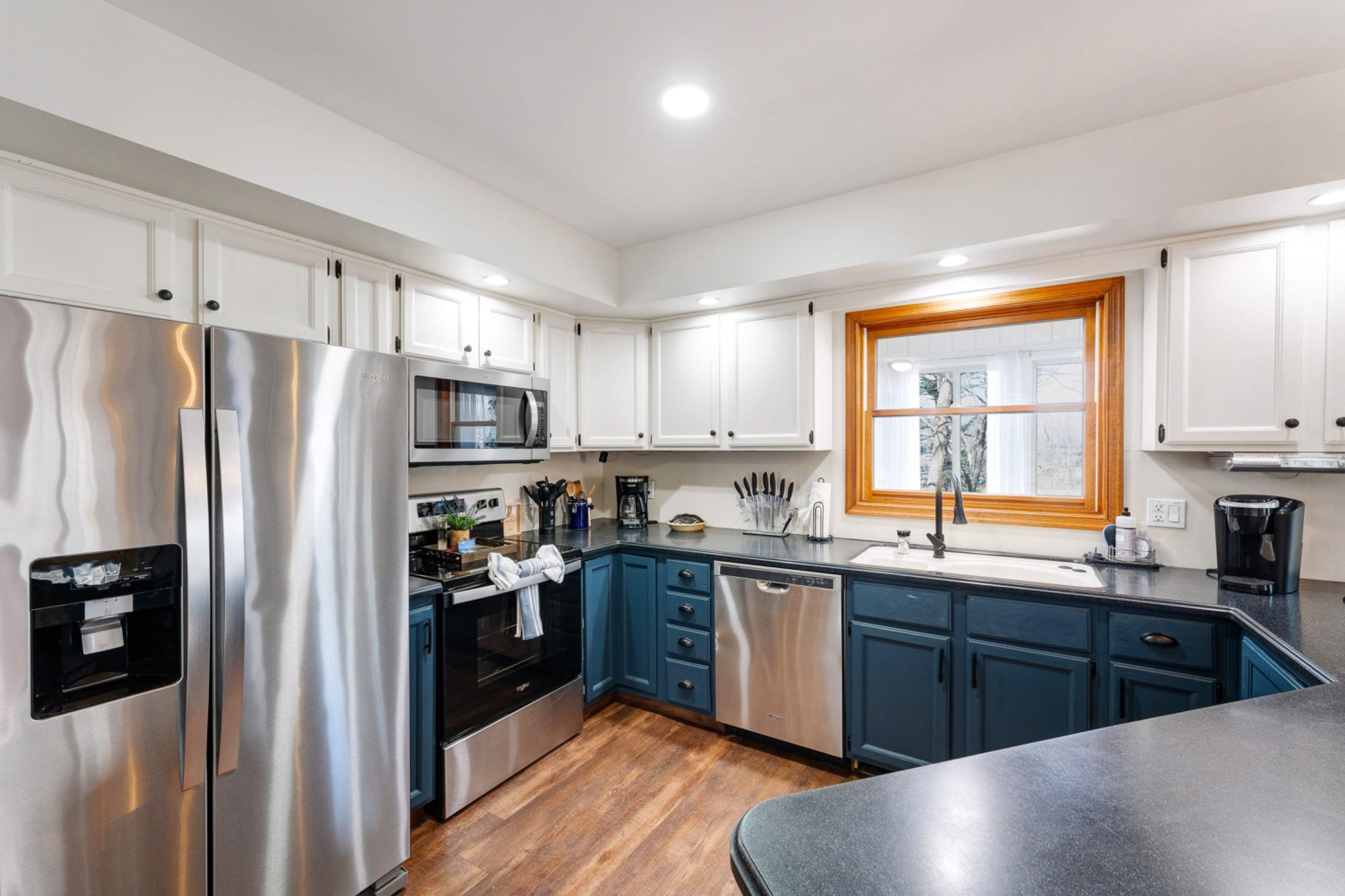 A modern kitchen with stainless steel appliances, blue cabinetry, and a wooden-framed window.