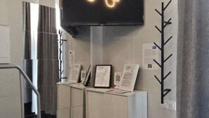 Un espace d’accueil moderne doté d’un téléviseur à écran plat affichant un logo, d’un porte-manteau et d’un escalier menant à un autre étage.