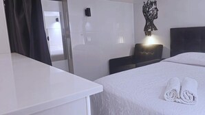 Une chambre d’hôtel avec un lit bien fait, une table de chevet, une chaise et un luminaire fixé au mur.