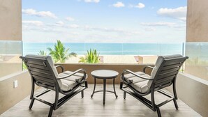Ein Balkon mit zwei Stühlen und einem kleinen Tisch, mit Blick auf einen Strand mit Palmen und den Ozean.