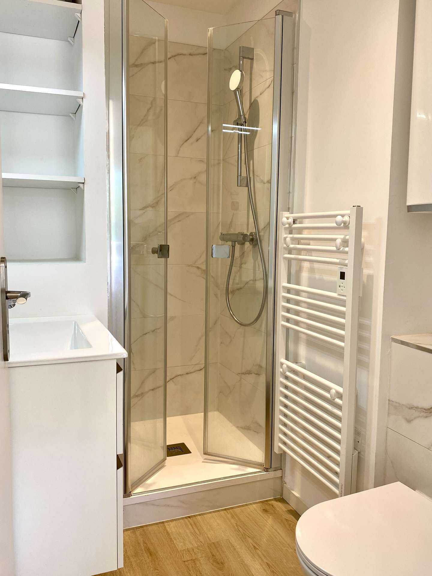 Ein modernes Badezimmer mit Duschkabine aus Glas, einem weißen Waschbecken und einem fest installierten Handtuchhalter.