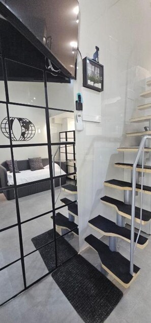 Une chambre d’hôtel moderne avec une cloison en verre, un lit, un escalier et un tableau encadré au mur.