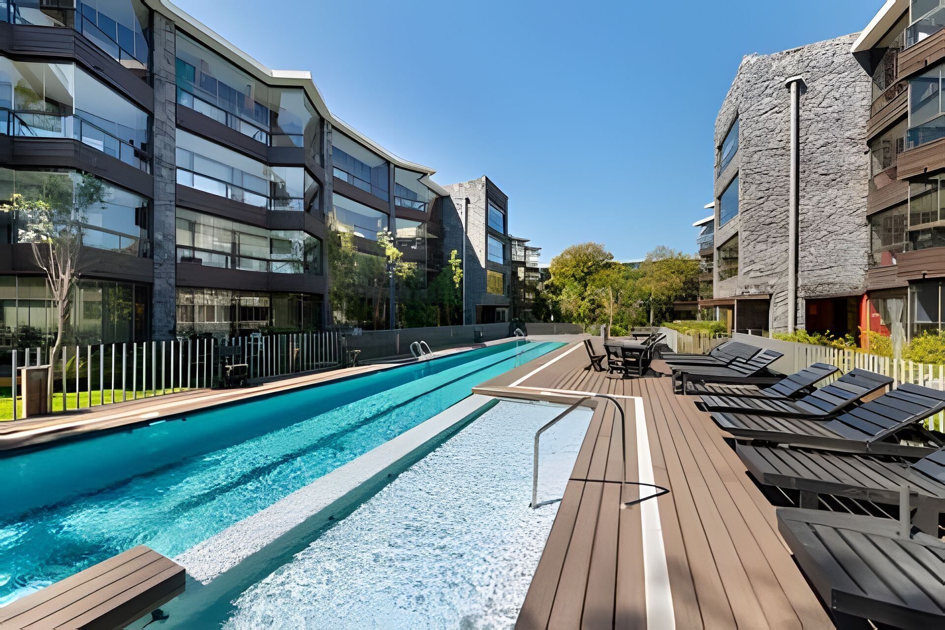 A modern pool area with a long swimming pool, wooden deck, and lounge chairs.