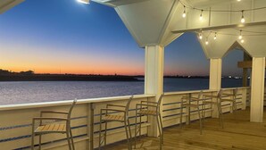 A covered deck with wooden flooring and metal chairs, overlooking a body of water at sunset. - Coastal Resort Stay | Walk to Beach | Pet-Friendly (Corpus Christi)