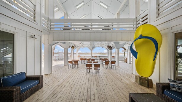 An indoor area with a high ceiling, wooden flooring, and a view of the beach. There are tables and chairs arranged for dining. - Coastal Resort Stay | Walk to Beach | Pet-Friendly (Corpus Christi)