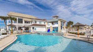 A swimming pool with a slide, lounge chairs, and a building with a thatched roof. - Coastal Resort Stay | Walk to Beach | Pet-Friendly (Corpus Christi)