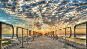 A coastal walkway with metal railings and a concrete path leading to the sea under a cloudy sky. - Coastal Resort Stay | Walk to Beach | Pet-Friendly (Corpus Christi)