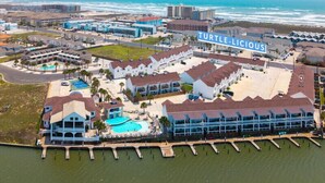 A coastal hotel with multiple buildings, a swimming pool, and a dock extending into the water. - Coastal Resort Stay | Walk to Beach | Pet-Friendly (Corpus Christi)