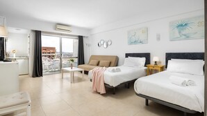 A hotel room with two beds, a sofa, a small table, and a balcony with a view.
