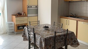 A compact kitchen with a dining table, chairs, a built-in oven, and a TV mounted above the oven. - Twins Apartment - Rodi Garganico (Rodi Garganico)