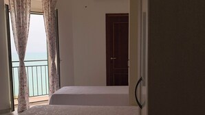 A room with a bed, a door, and a view of the sea through a window with curtains. - Twins Apartment - Rodi Garganico (Rodi Garganico)