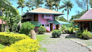 A two-story house with a balcony, surrounded by tropical vegetation and palm trees. - Fare Manu (Moorea-Maiao)