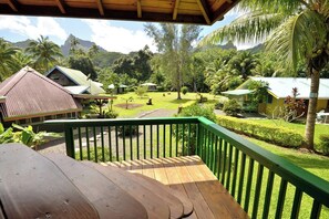 A wooden deck with a green railing overlooking a lush garden with palm trees and a mountain in the background. - Fare Manu (Moorea-Maiao)