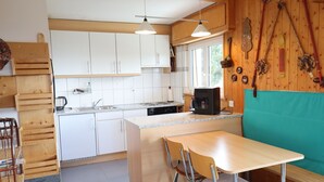 Een kleine keuken met witte kastjes, een houten eettafel en een tealkleurige bank met kussens.