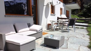 Een terras met een rieten bank en stoelen, een tafel en een salontafel met glazen blad.