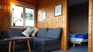 Een gezellige kamer met een grijze bank, een klein houten tafeltje en een bed met een blauwe deken.