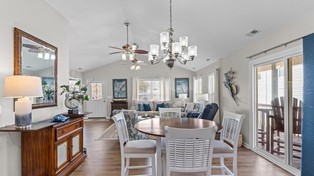 A spacious dining area with a round table and white chairs, a wooden cabinet, and a chandelier. - Charming 3BR, 2BA Canal-Front Getaway with Kayaks in Oak Island, NC! (Oak Island)
