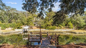 A wooden bridge over a pond with a wooden deck and a building in the background. - Charming 3BR, 2BA Canal-Front Getaway with Kayaks in Oak Island, NC! (Oak Island)