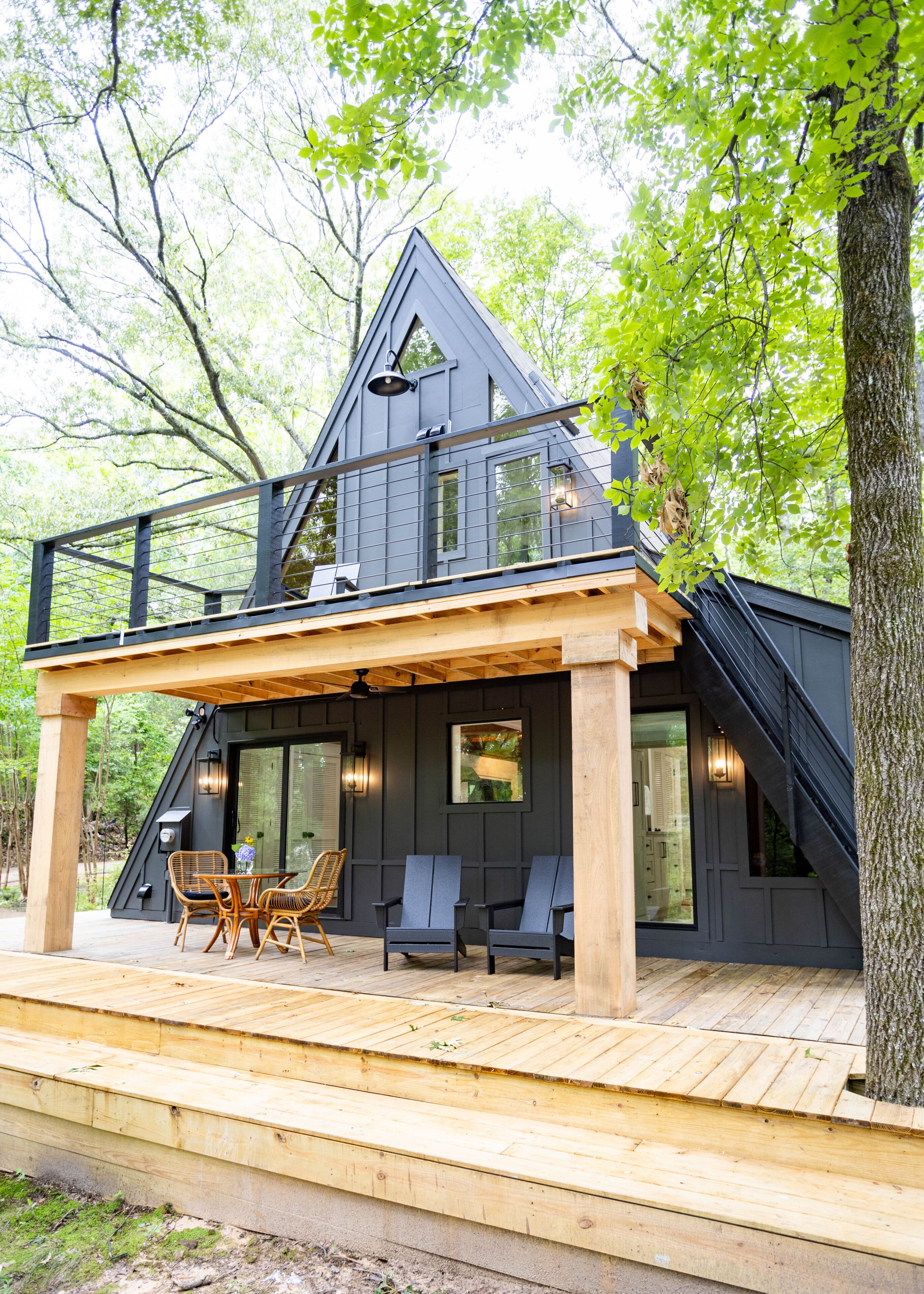 A modern cabin with a wooden deck, outdoor seating, and large windows.