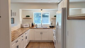 A modern kitchen with white cabinets, a wooden countertop, a built-in microwave, and a refrigerator. - SILVERWOOD•Hot Tub•Lake Fun•Family Friendly•CLEAN! (Hayden)