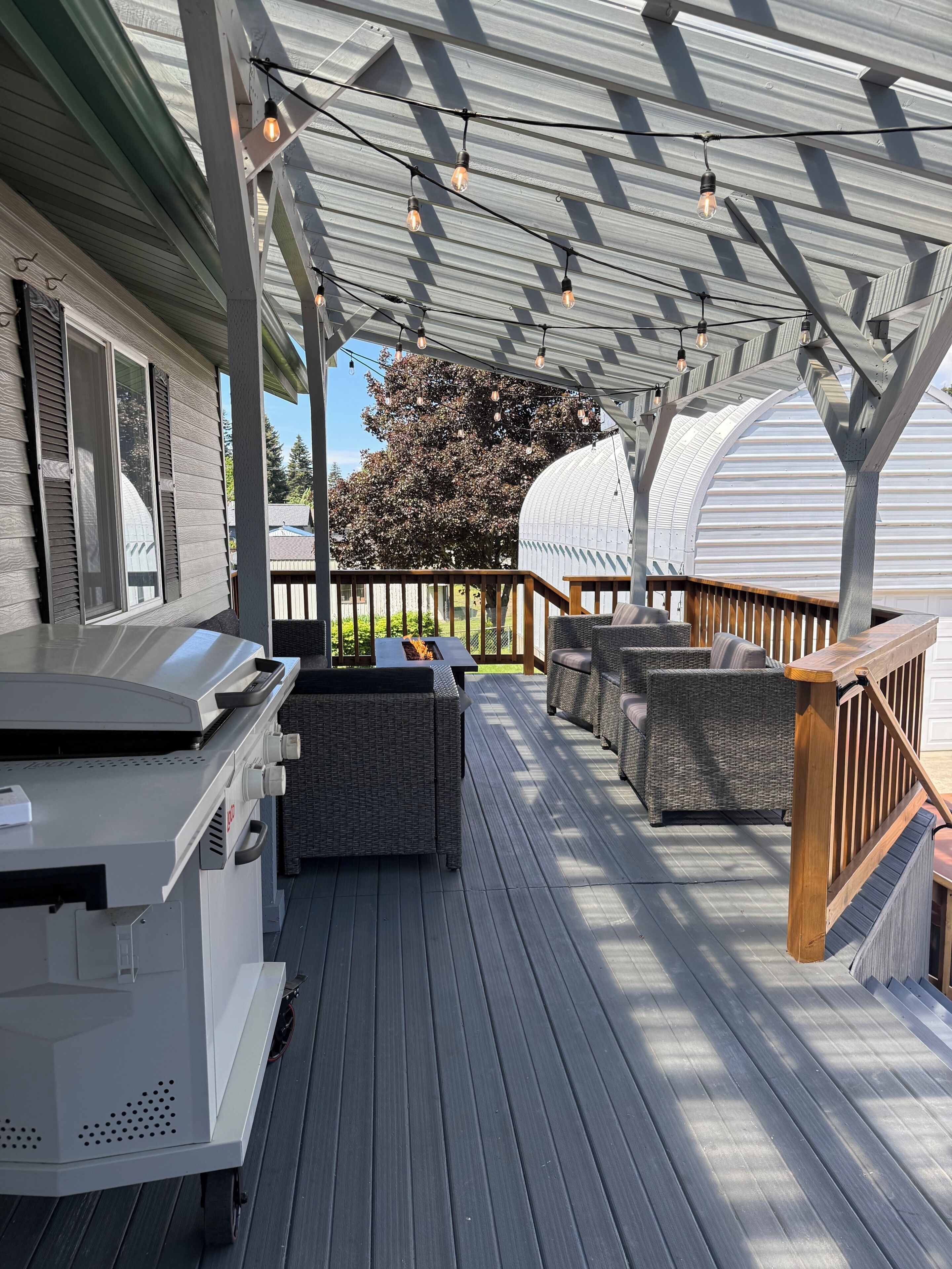 A covered deck with outdoor furniture, a grill, and string lights.