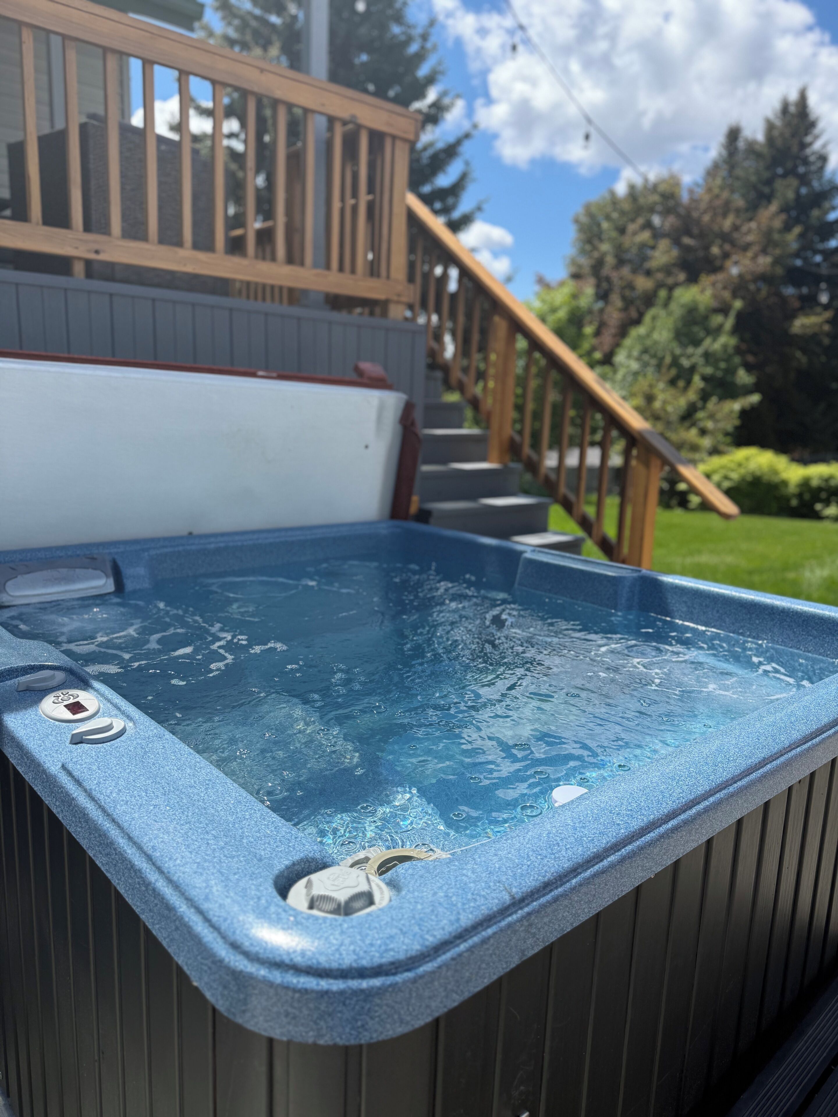 Un jacuzzi con botones de control, una terraza de madera y una escalera que lleva a un área cubierta.