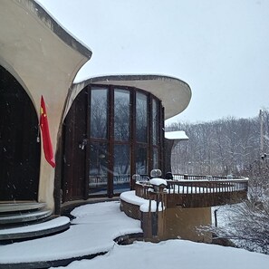 Un edificio con un amplio ventanal y ventanas, una bandera a la izquierda y un porche cubierto de nieve.