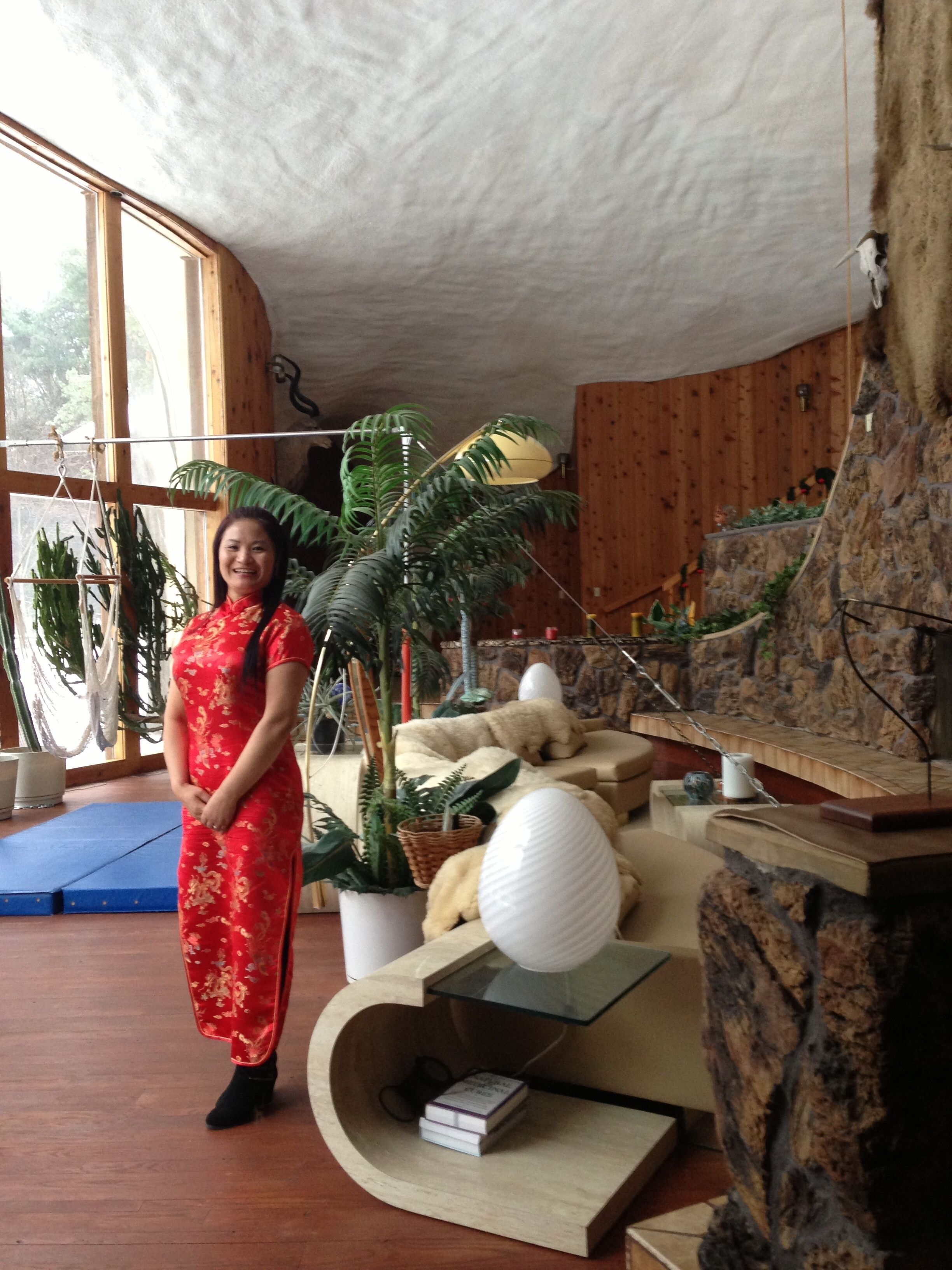 Una habitación con un ventanal grande, una planta en maceta, un objeto esférico blanco y una estructura de madera.
