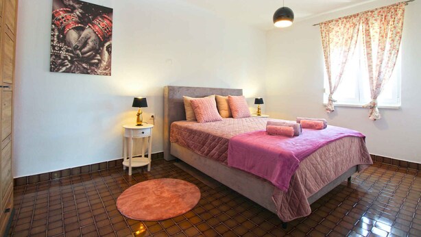 A bedroom with a bed, two bedside tables, a round rug, a painting on the wall, and a window with curtains. - Holiday apartment with a/c (Pula)