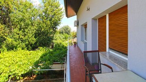 A balcony with a table and chair, a potted plant, and a view of greenery and trees. - Holiday apartment with a/c (Pula)