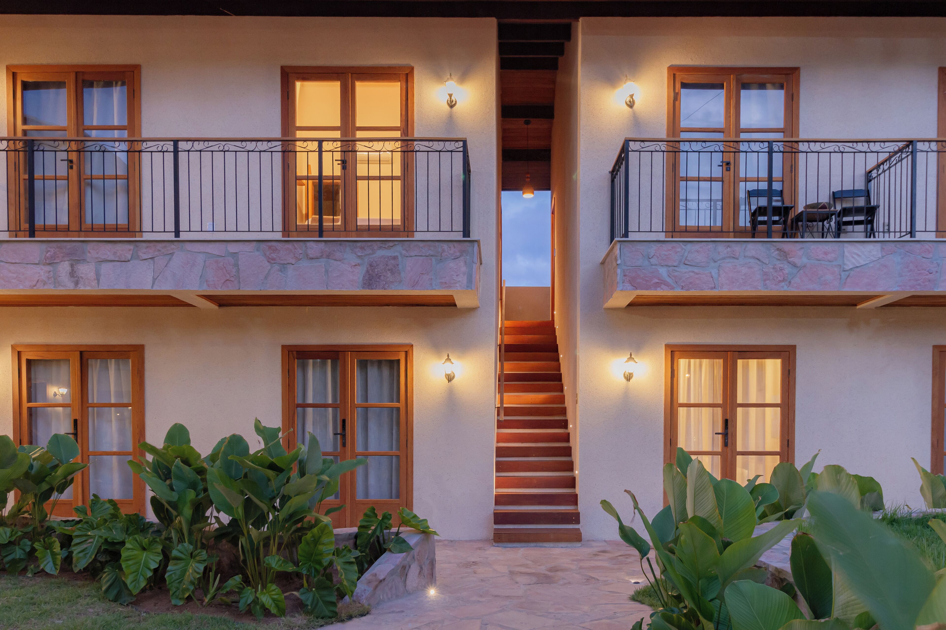 A two-story building with a central staircase, balconies with railings, and large windows with curtains.