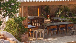 An outdoor patio with stone tables and chairs, a pool, and a stone wall. - Moã Charme Hotel (Mucuge)