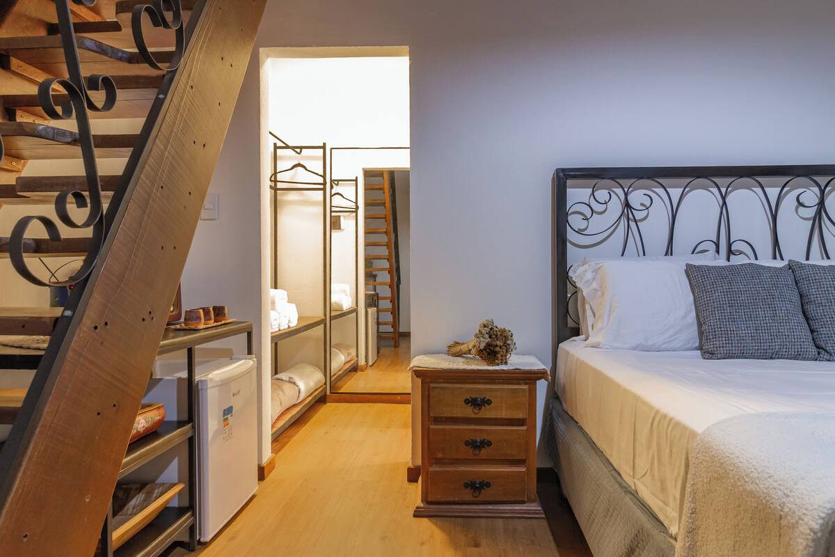 A bedroom with a bed, a nightstand, a dresser, a wardrobe, and a staircase.