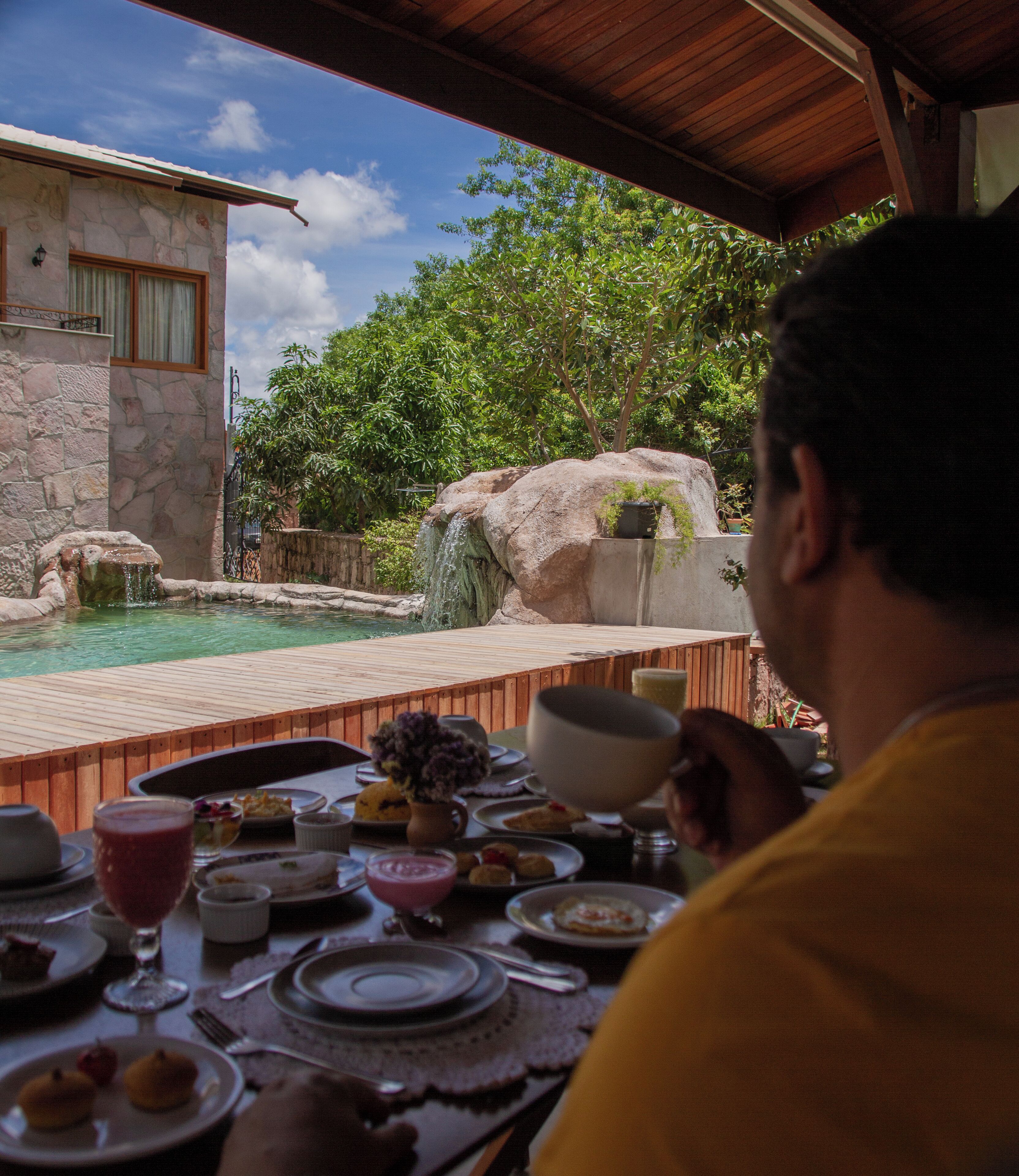 A dining area with a view of a swimming pool and a stone building.