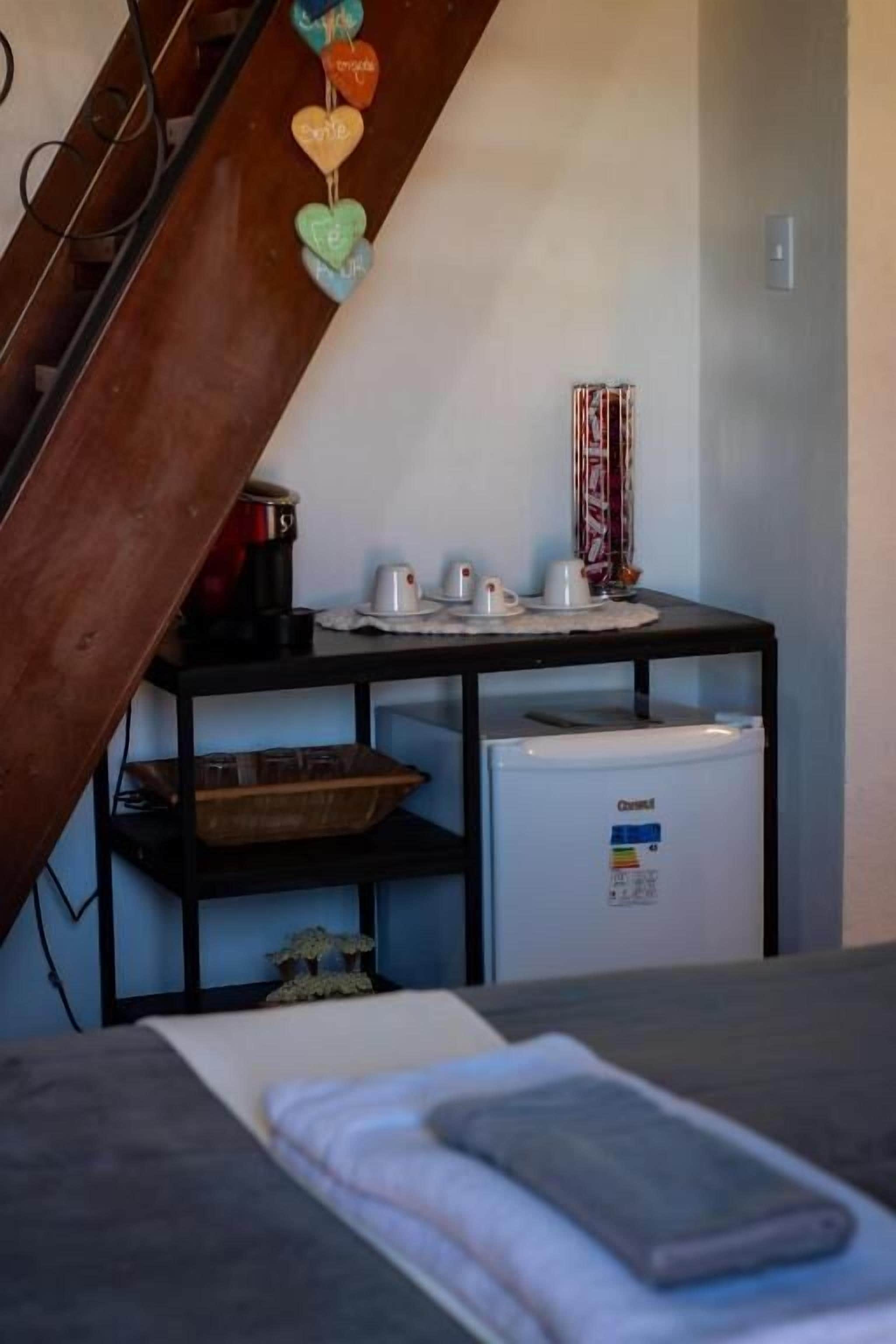 Uma cozinha com geladeira, cafeteira e chaleira em bancada preta.