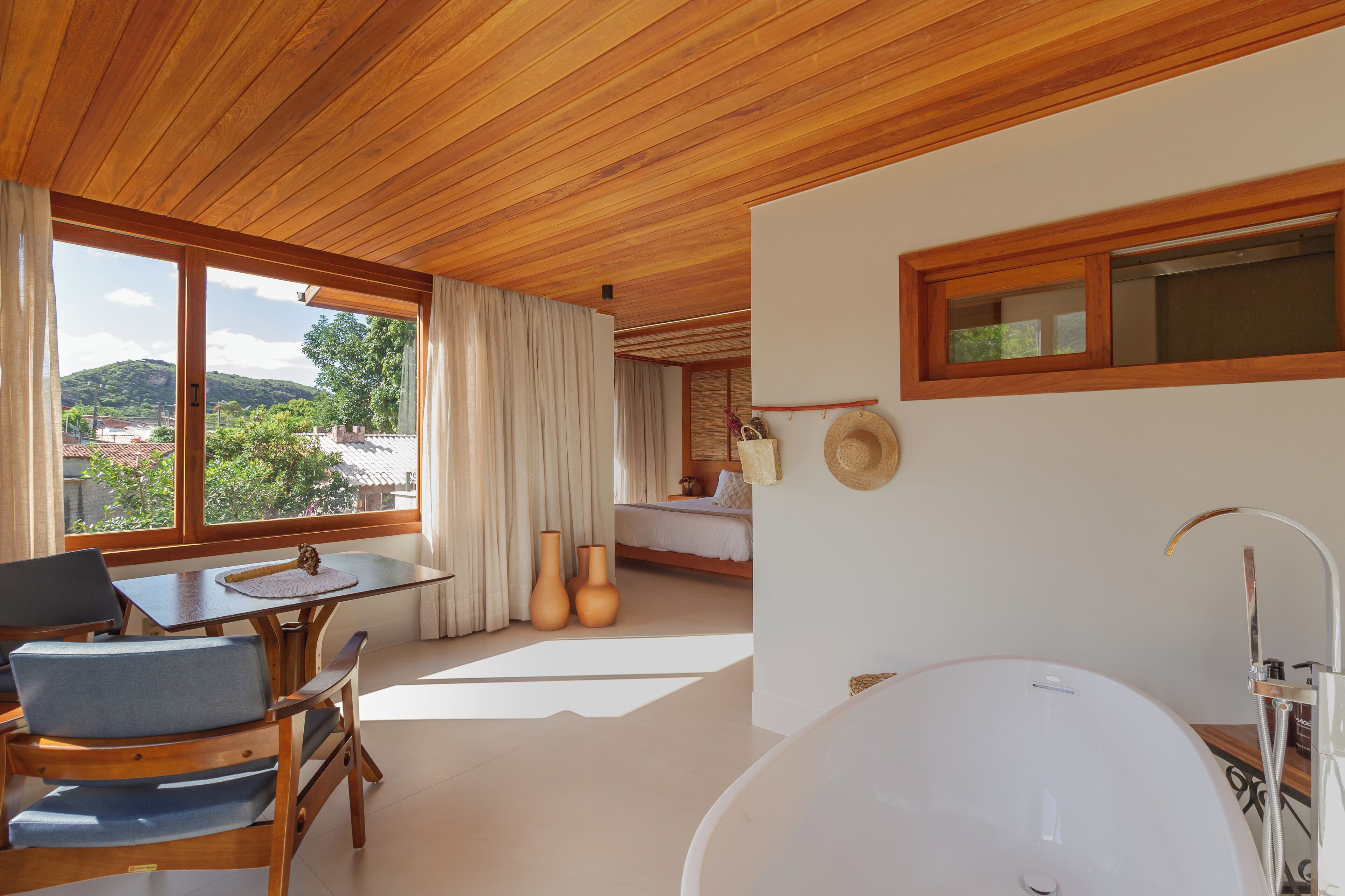Un baño moderno con una bañera grande, techo de madera y ventanas amplias que ofrecen vistas al exterior.