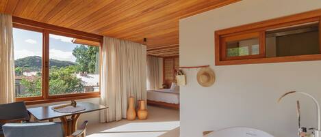 Un baño moderno con una bañera grande, techo de madera y ventanas amplias que ofrecen vistas al exterior.