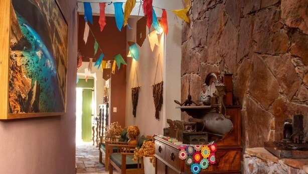 A narrow hallway with a rustic stone wall, wooden furniture, and colorful bunting. - Moã Charme Hotel (Mucuge)