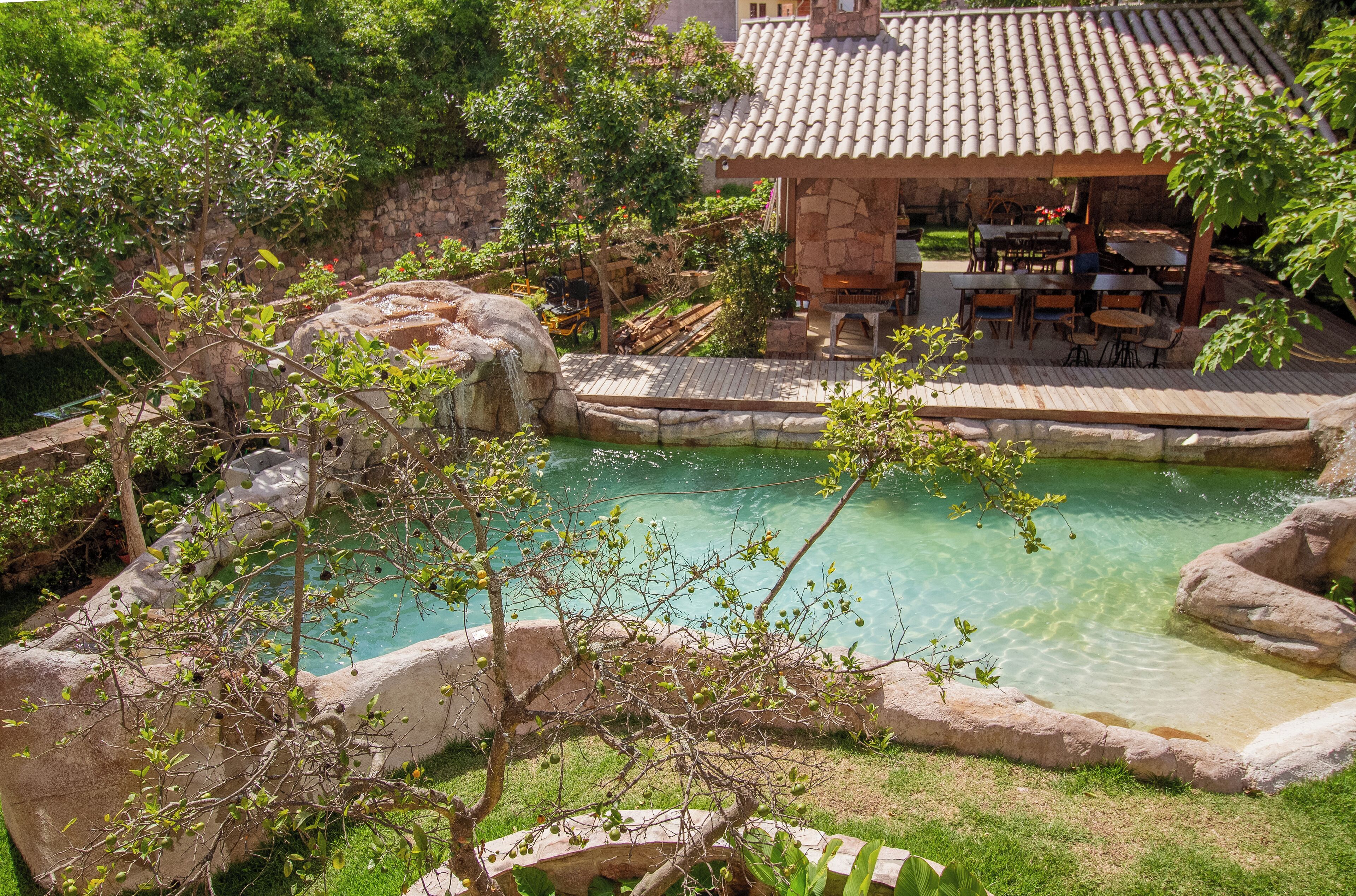 Área de piscina com estrutura de pedra, assentos e vegetação ao redor.