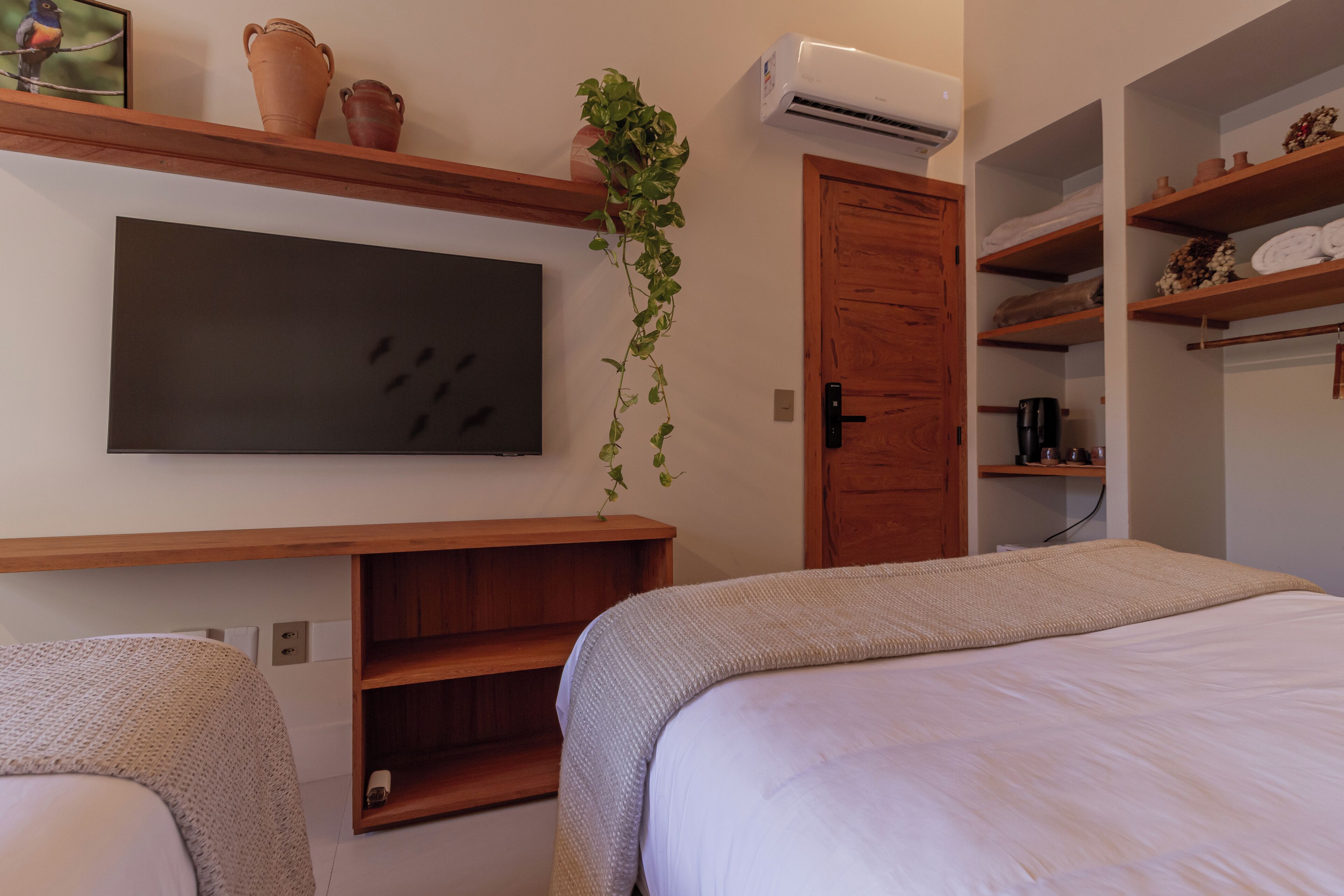 A bedroom with a bed, a TV, a plant, and shelves with toiletries.