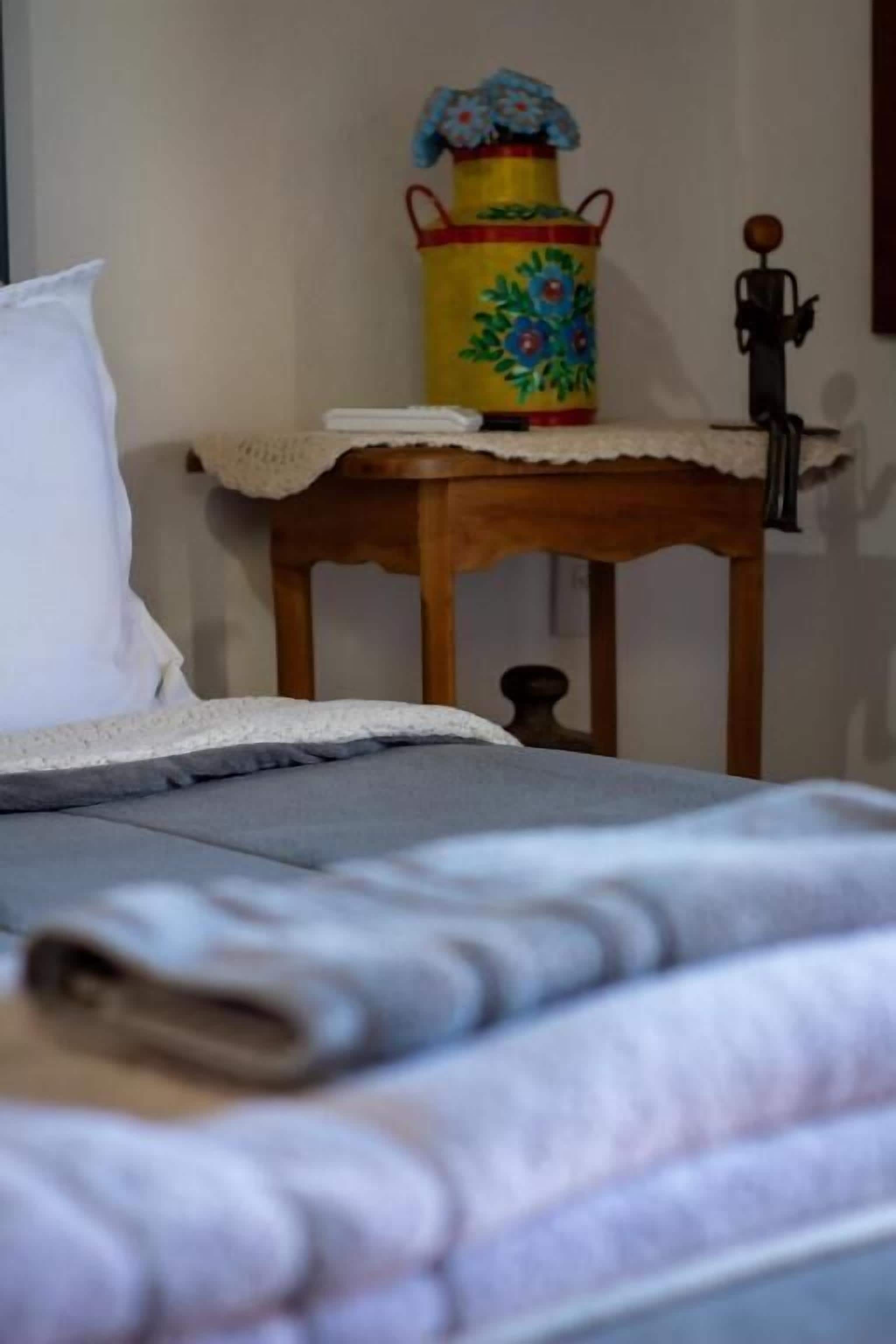 Un lit avec une couverture grise, un oreiller blanc et une table de chevet en bois ornée d’un objet décoratif et d’une petite figurine.