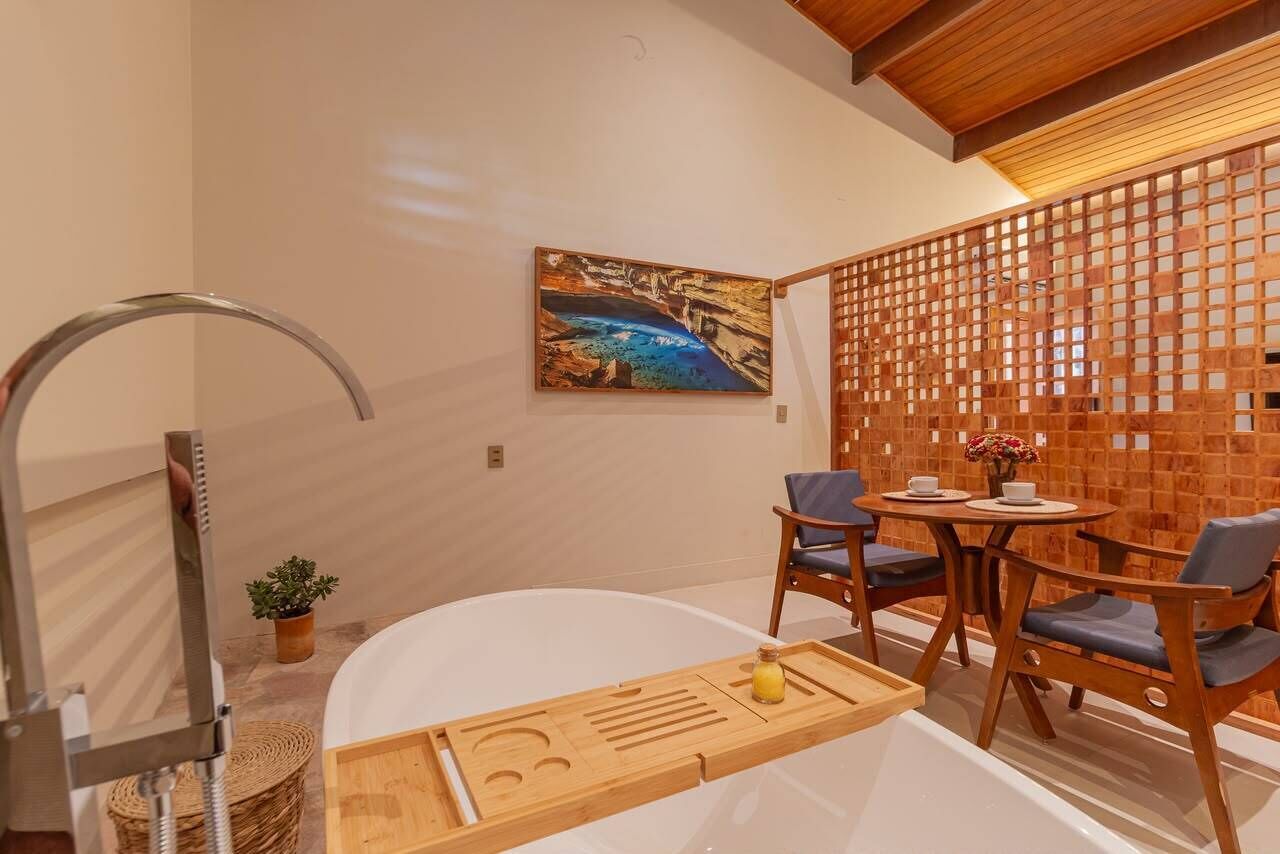 A modern bathroom with a bathtub, a wooden tray, and a seating area with chairs and a table.