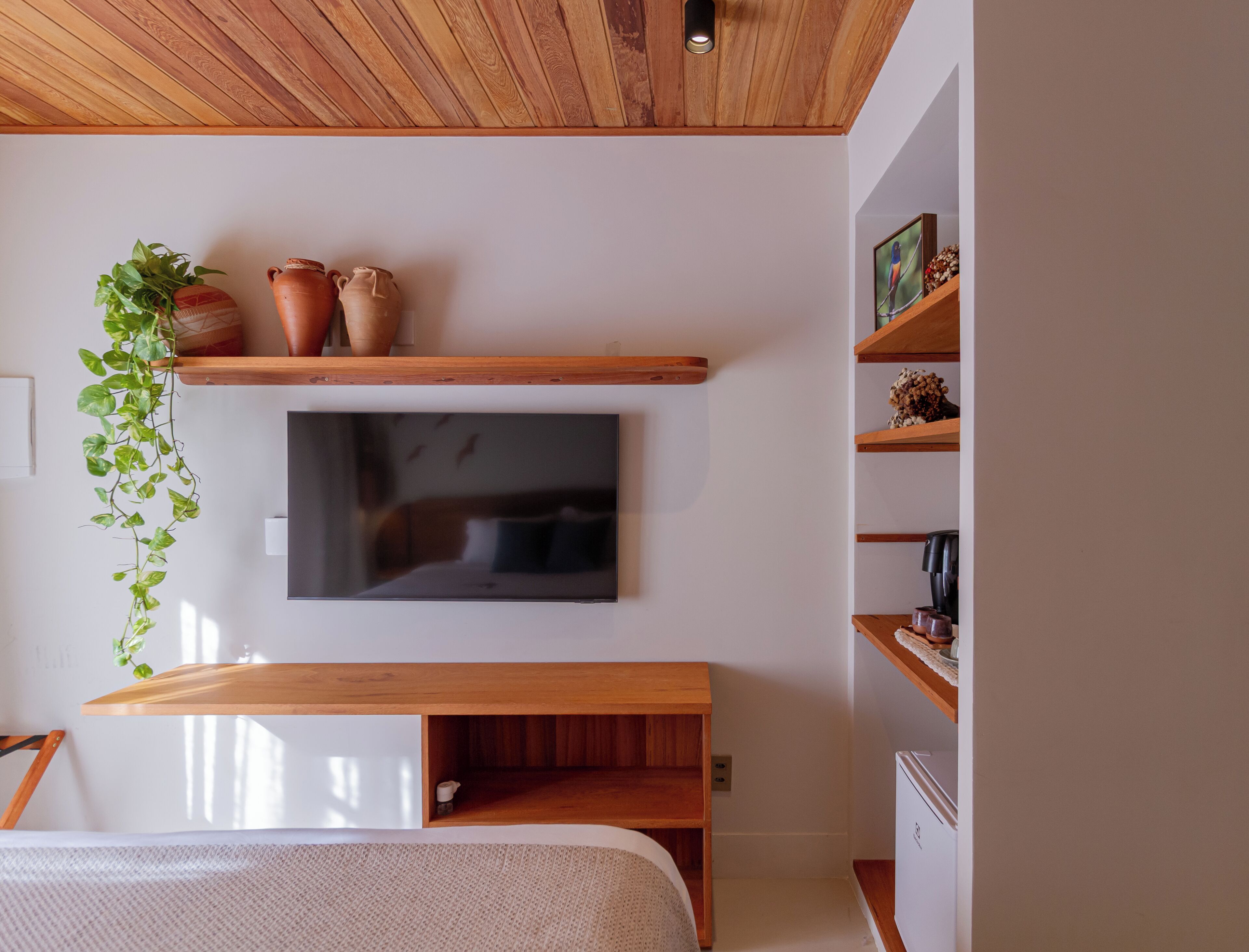 Une chambre avec un plafond en bois, un téléviseur fixé au mur, un lit, une table de chevet et une plante suspendue.