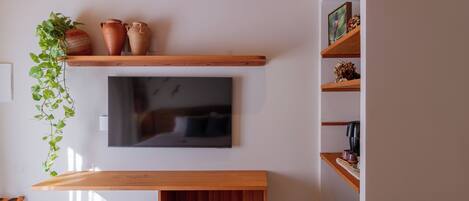 Une chambre avec un plafond en bois, un téléviseur fixé au mur, un lit, une table de chevet et une plante suspendue.
