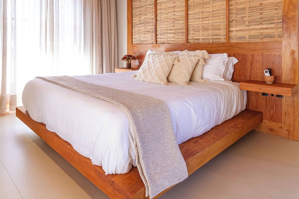 A spacious bedroom with a large bed, wooden headboard, and a woven ceiling.