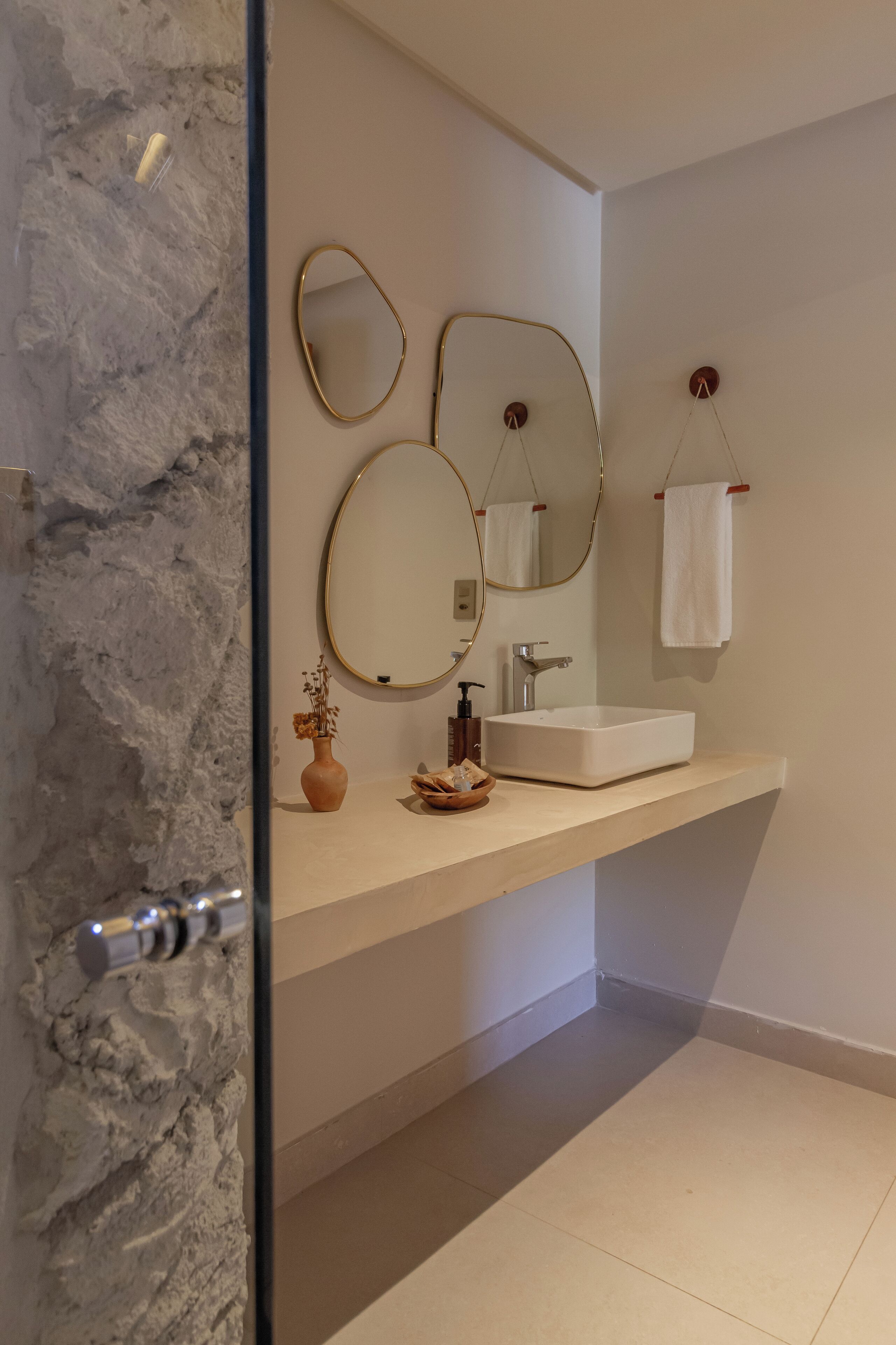 A modern bathroom with a marble wall, a white sink, and two mirrors.
