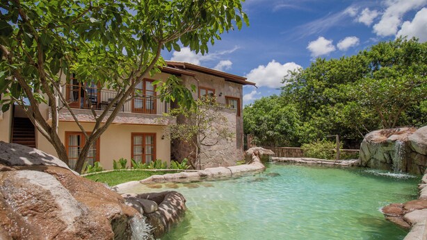 A two-story building with a pool, surrounded by greenery and a clear sky. - Moã Charme Hotel (Mucuge)