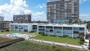 Un hotel a più piani con piscina, numerosi balconi e un prato curato.